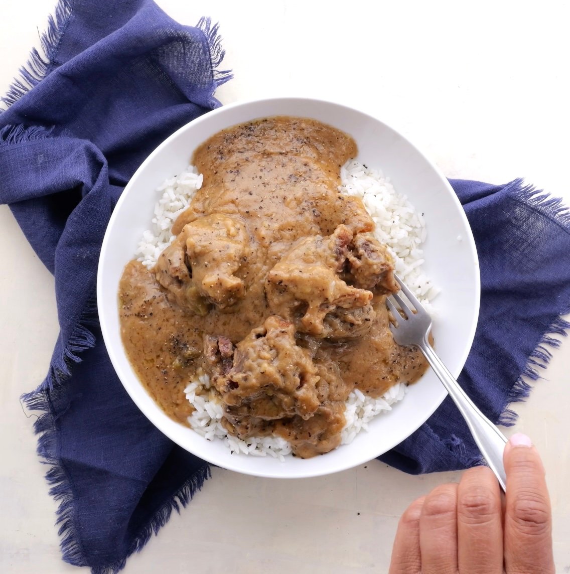 Oxtails in gravy with white rice in a white bowl.