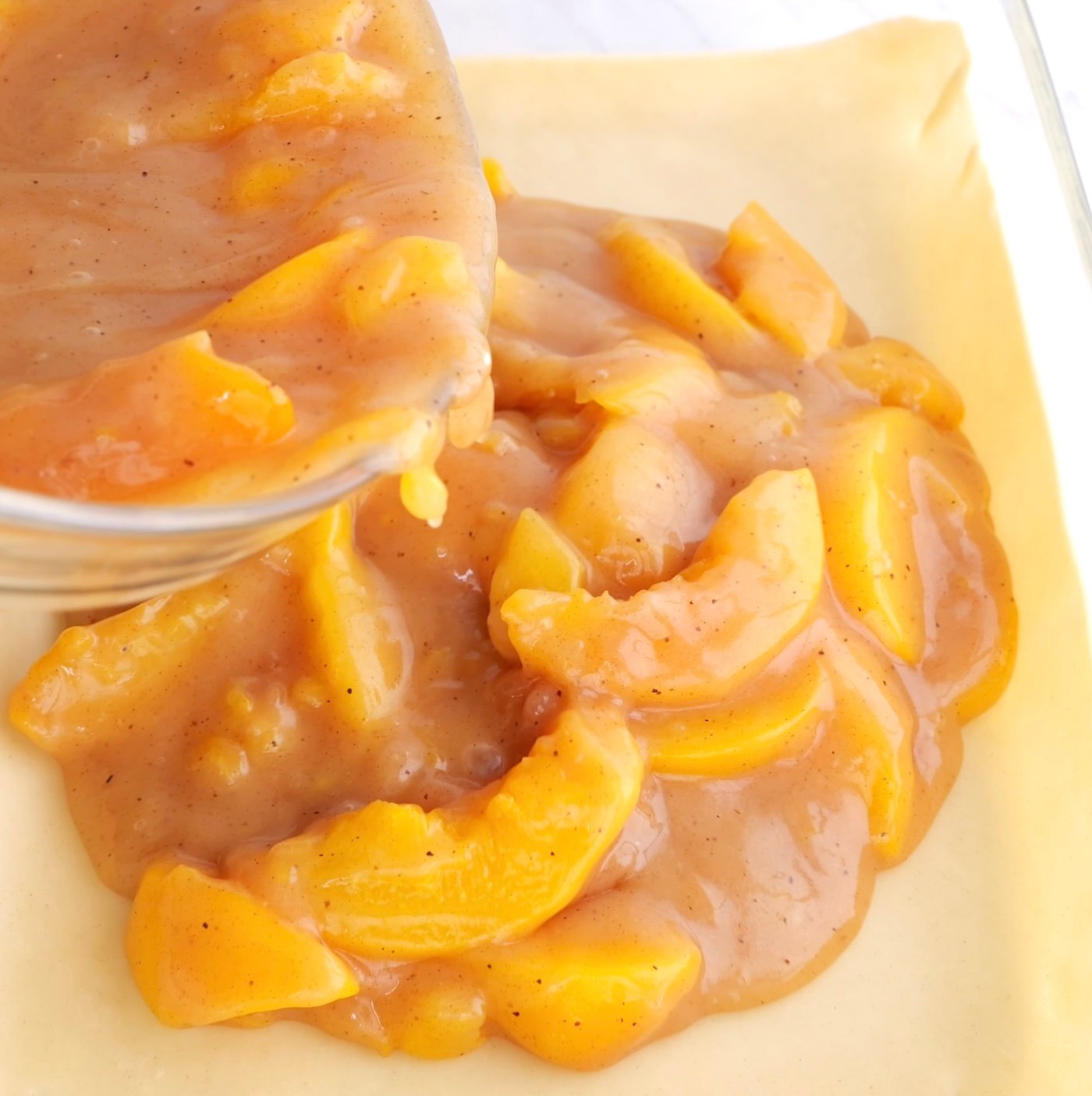 Pouring peach cobbler filling in a casserole dish lined with parchment paper.