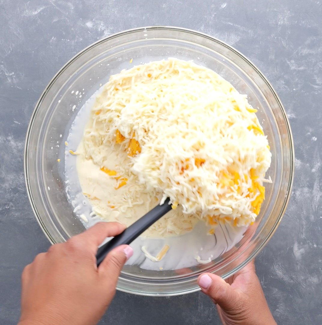 A hand folding in grated cheeses into the milk mixture.