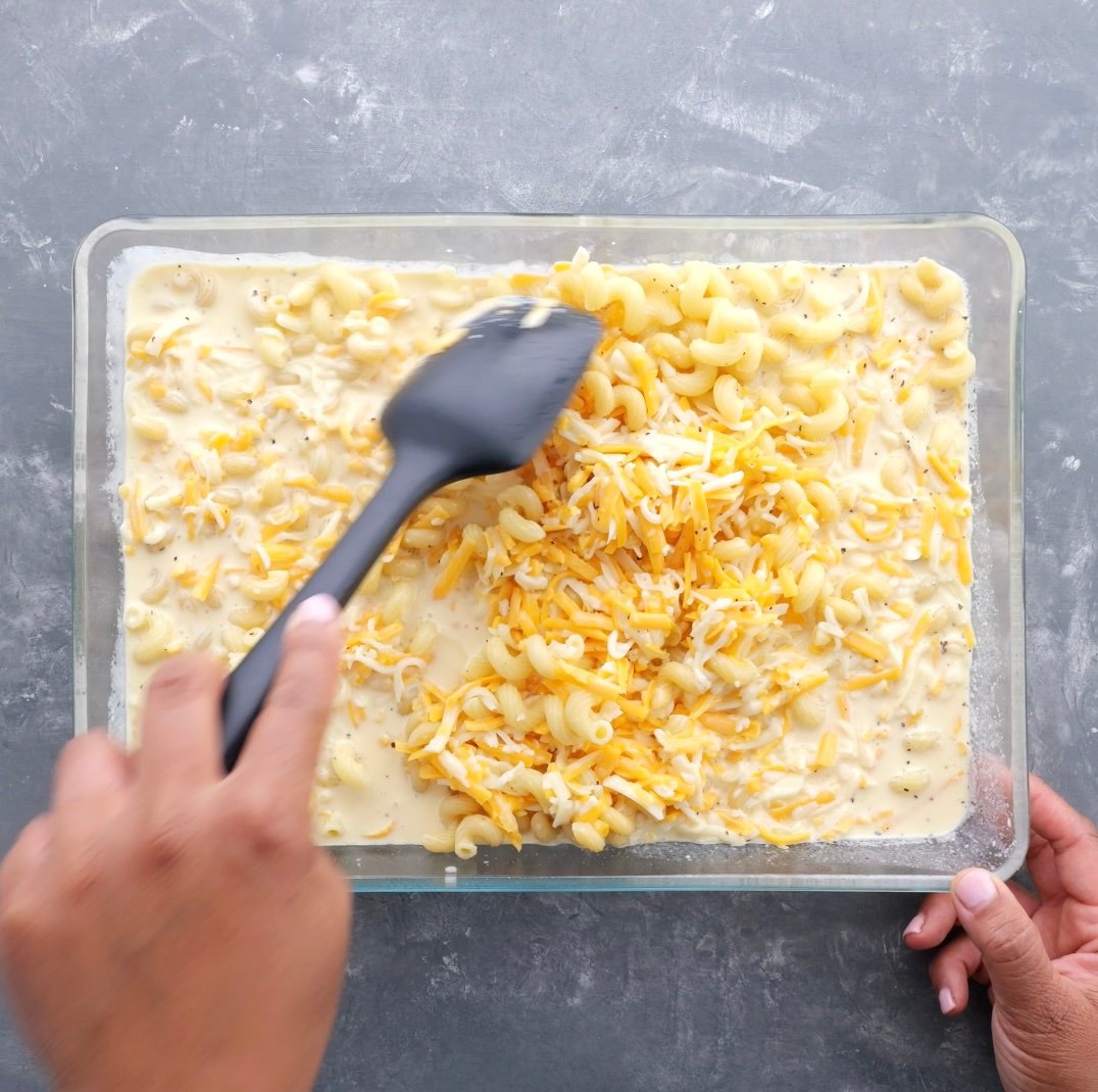 A baking dish with cheese and a hand spreading out the cheese over the noodles.