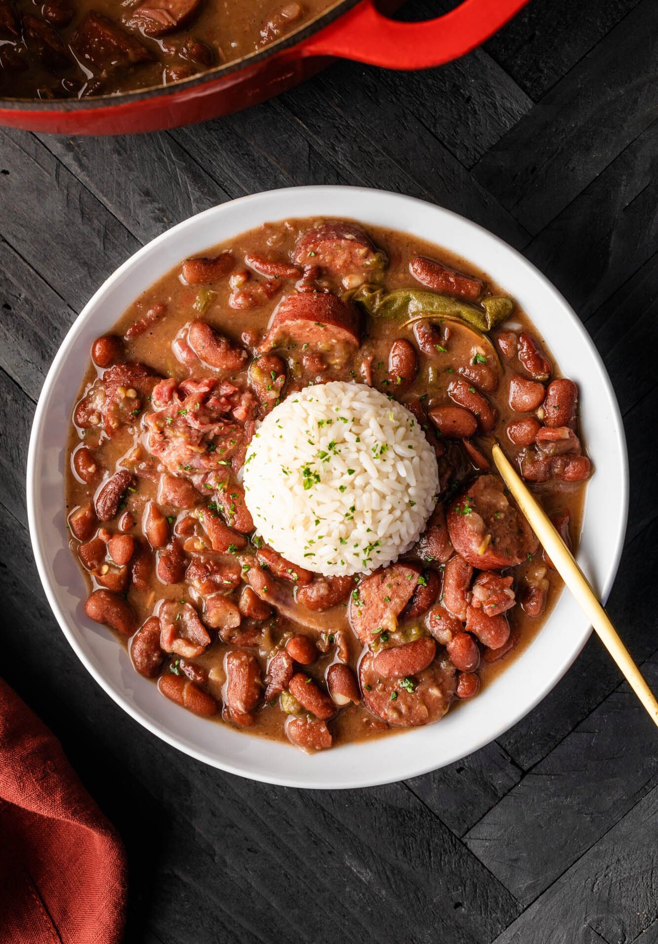 New Orleans red beans topped with rice in a white bowl on a black background.