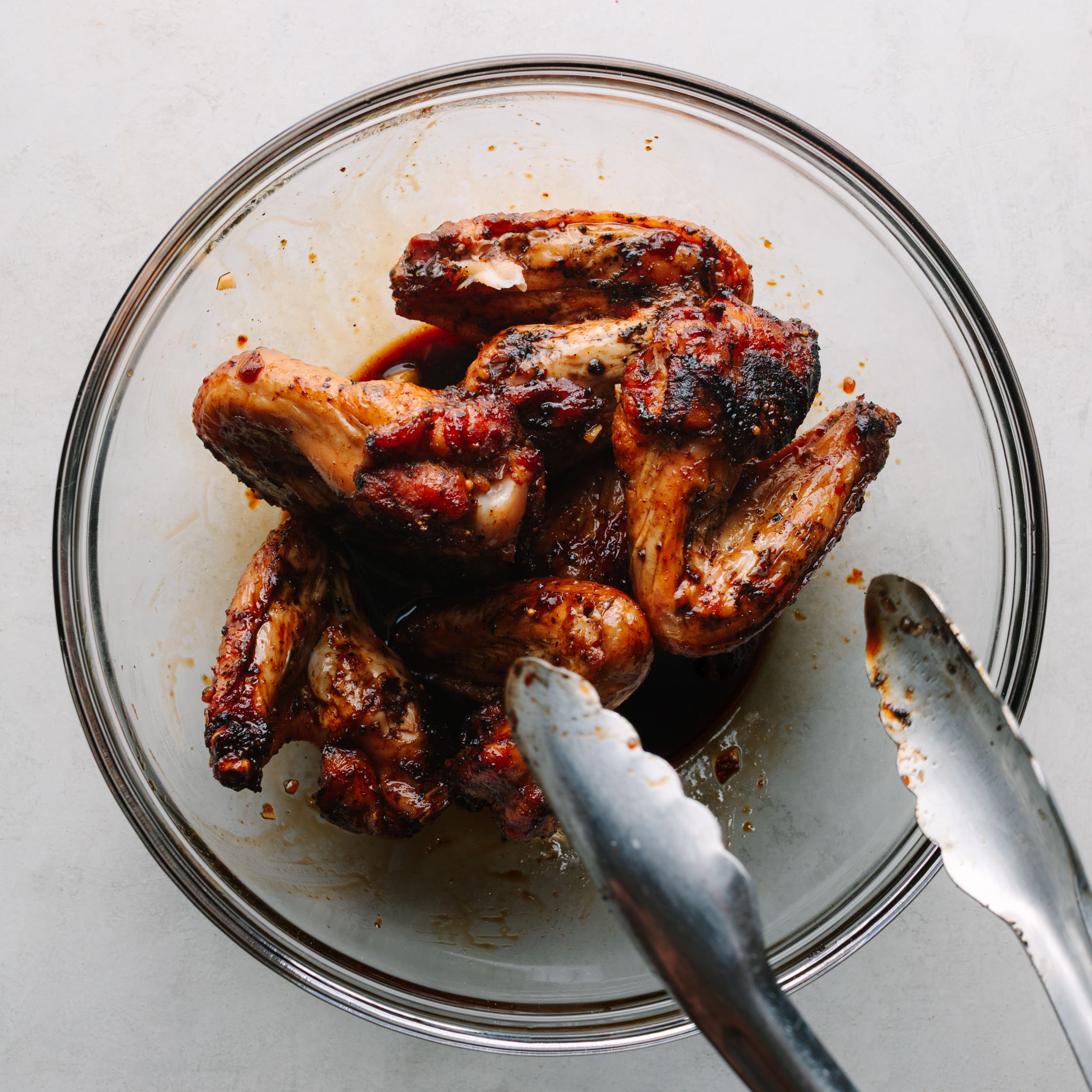 A clear glass bowl of Asian wings being tossed in Asian wing sauce. 