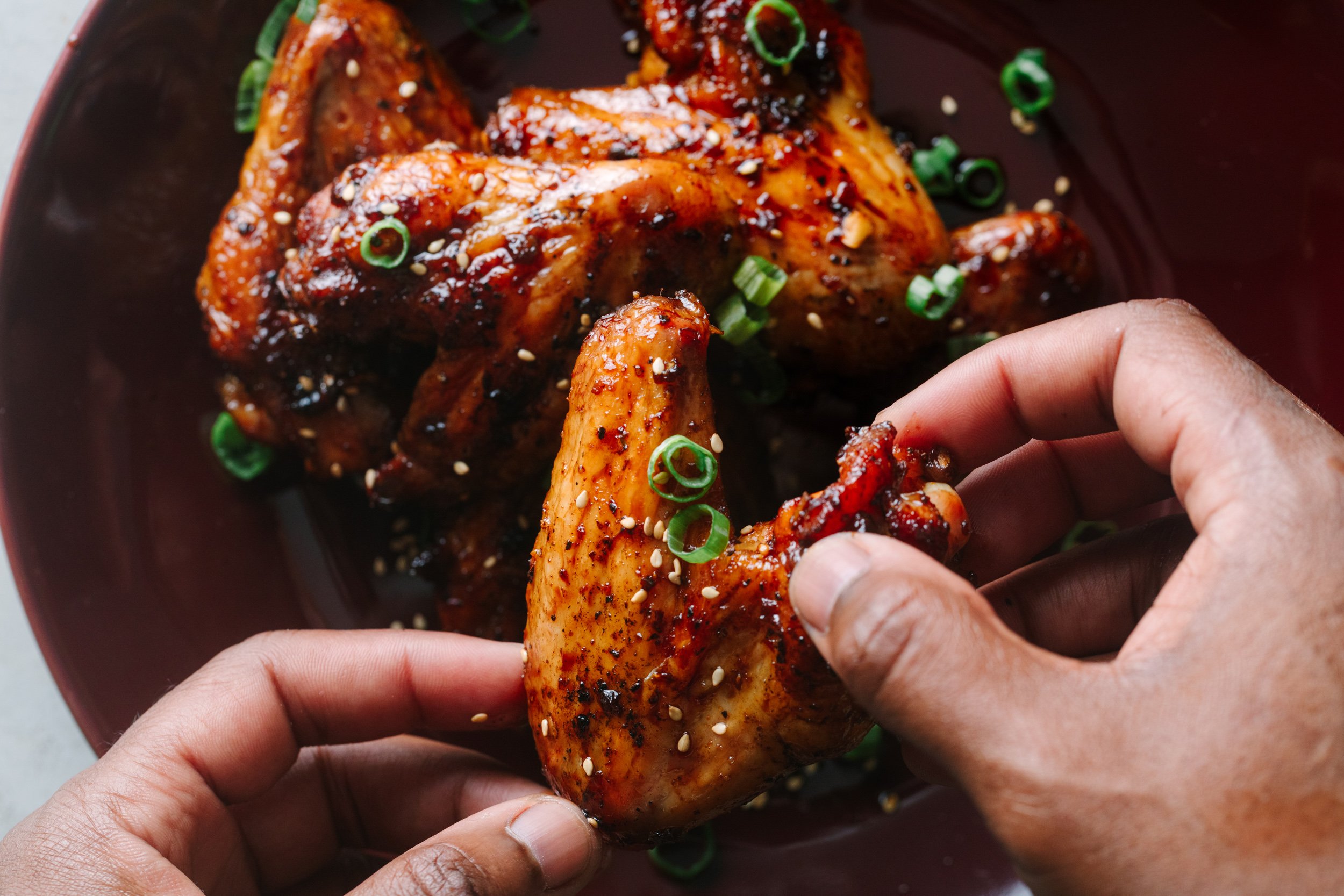 African American hands holding Asian chicken wings garnished with sesame seeds and green onions.