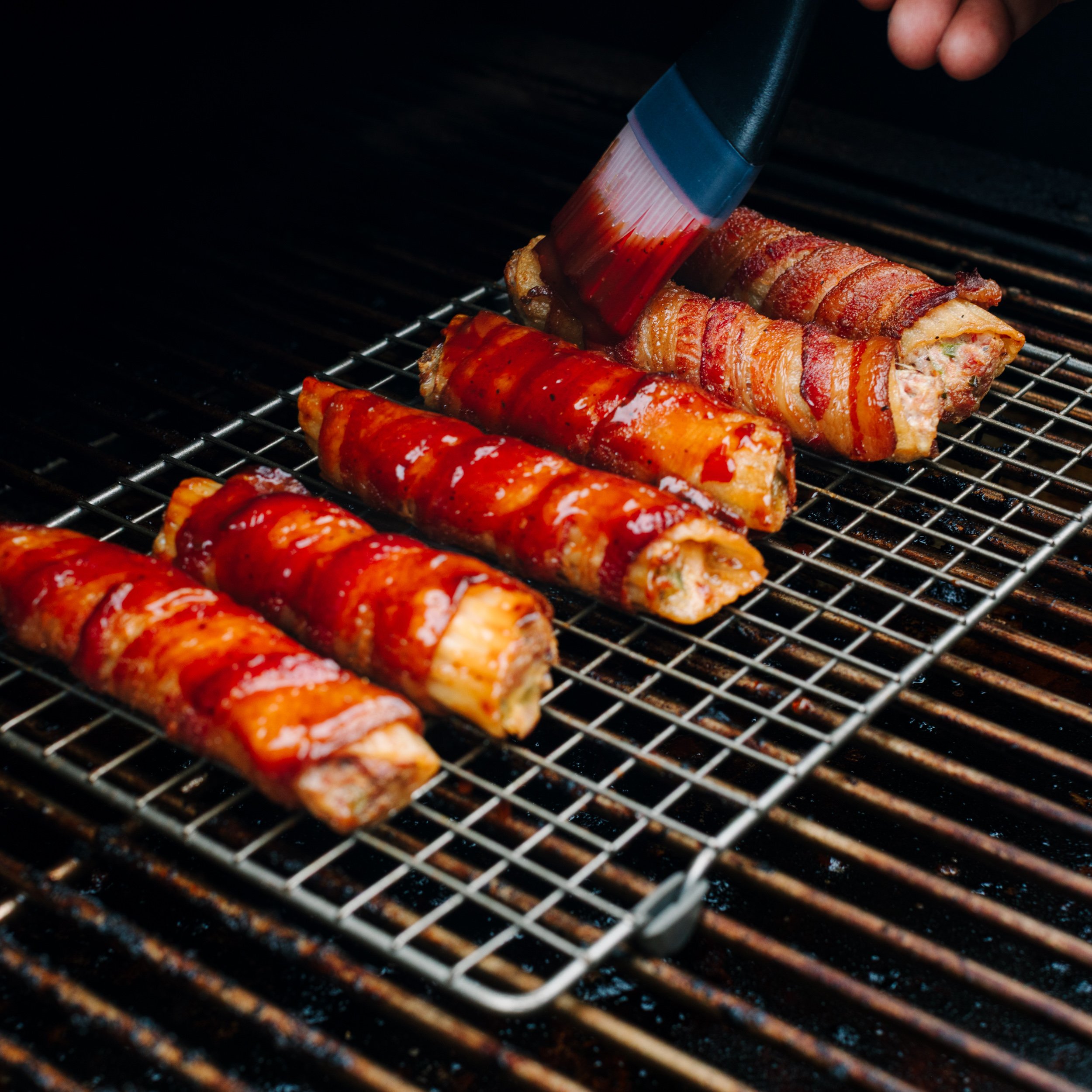 Smoked shotgun shells on a wire rack on a smoker being basted with BBQ sauce.