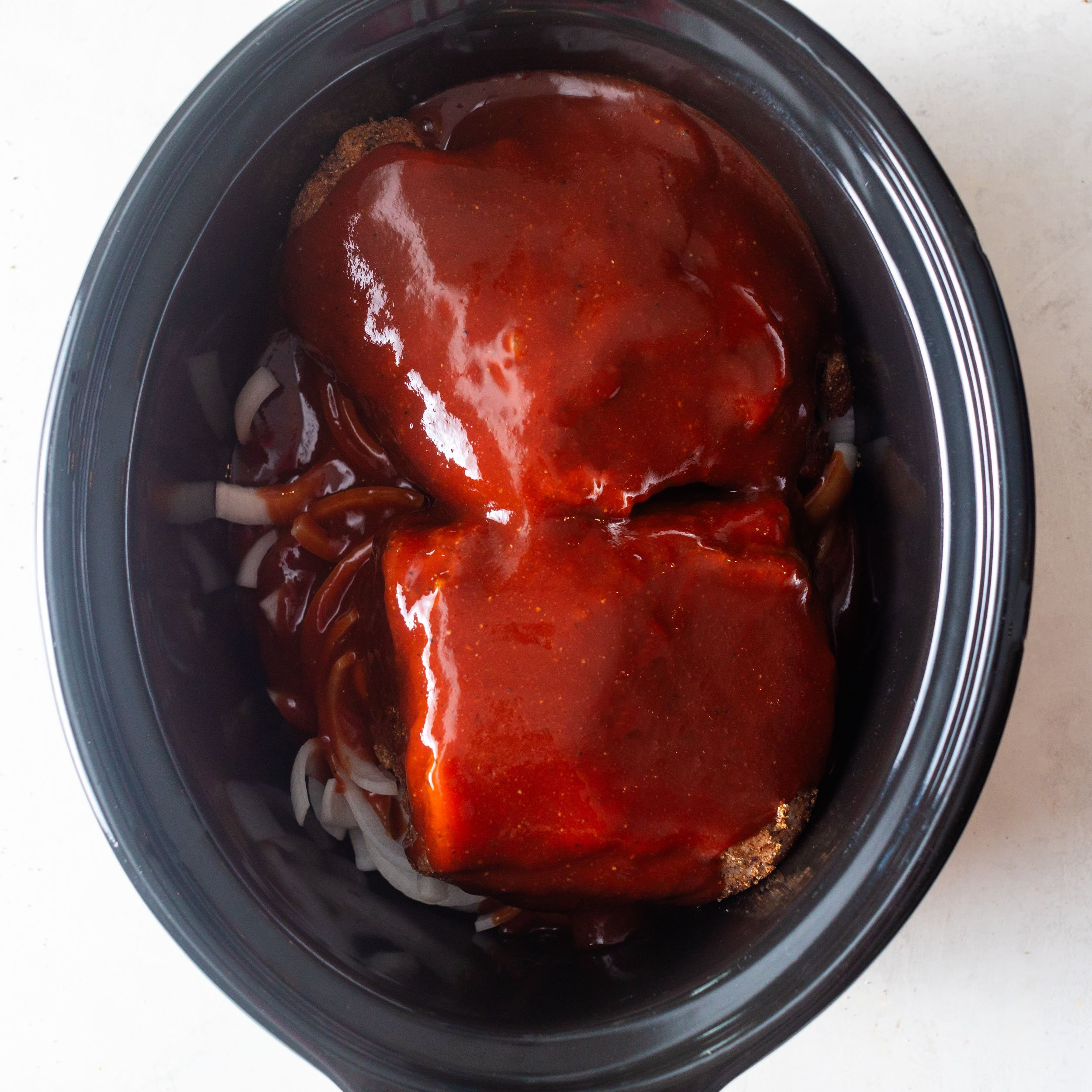 boneless pork shoulder in a slow cooker covered in bbq sauce with sliced white onions